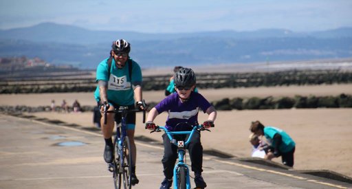 An adult and child rider together at the North Wales Coast Bikeathon