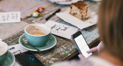 Person using phone and drinking coffee.
